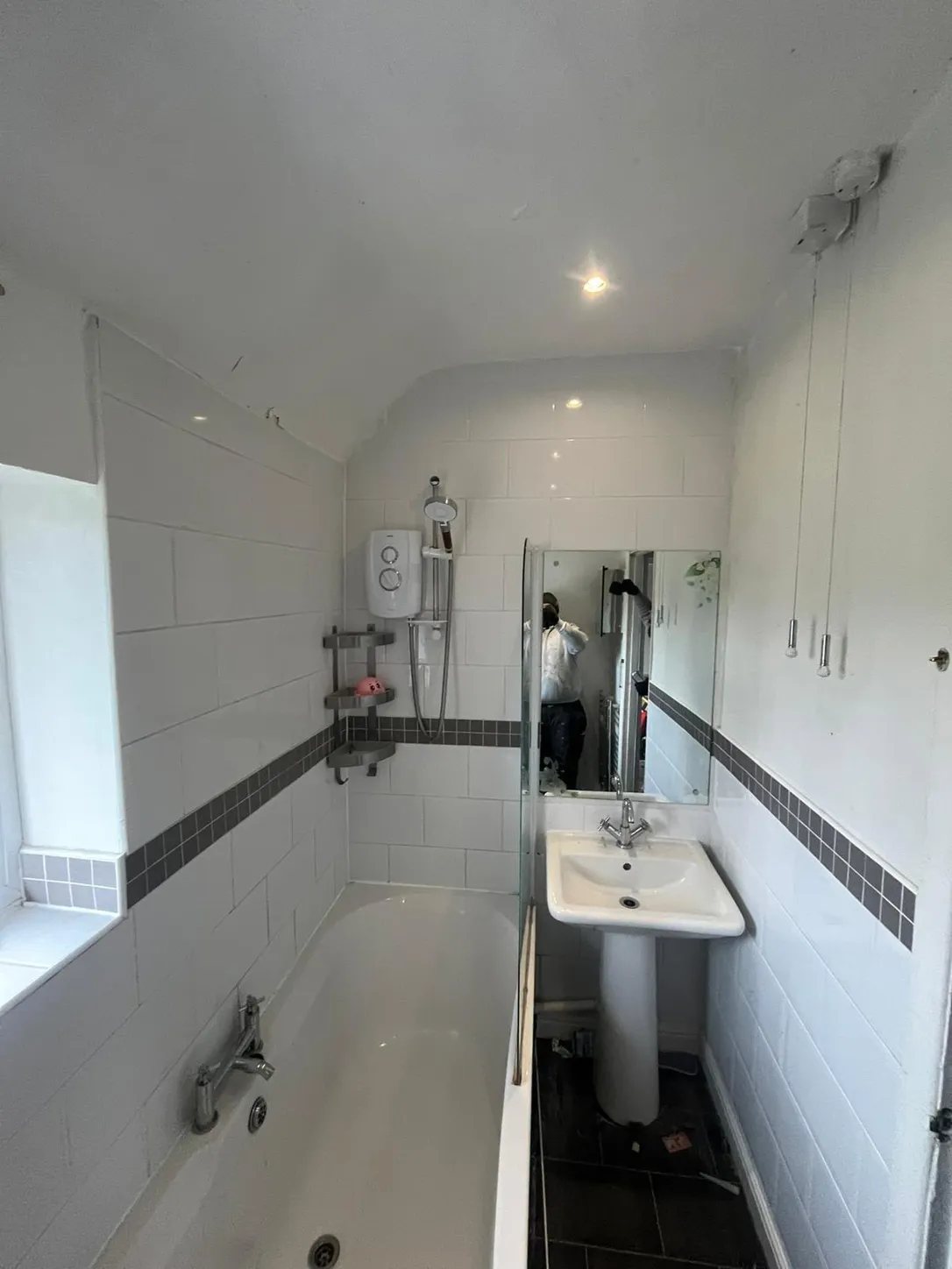 Same bathroom before: dated white tiles, old electric shower and pedestal basin