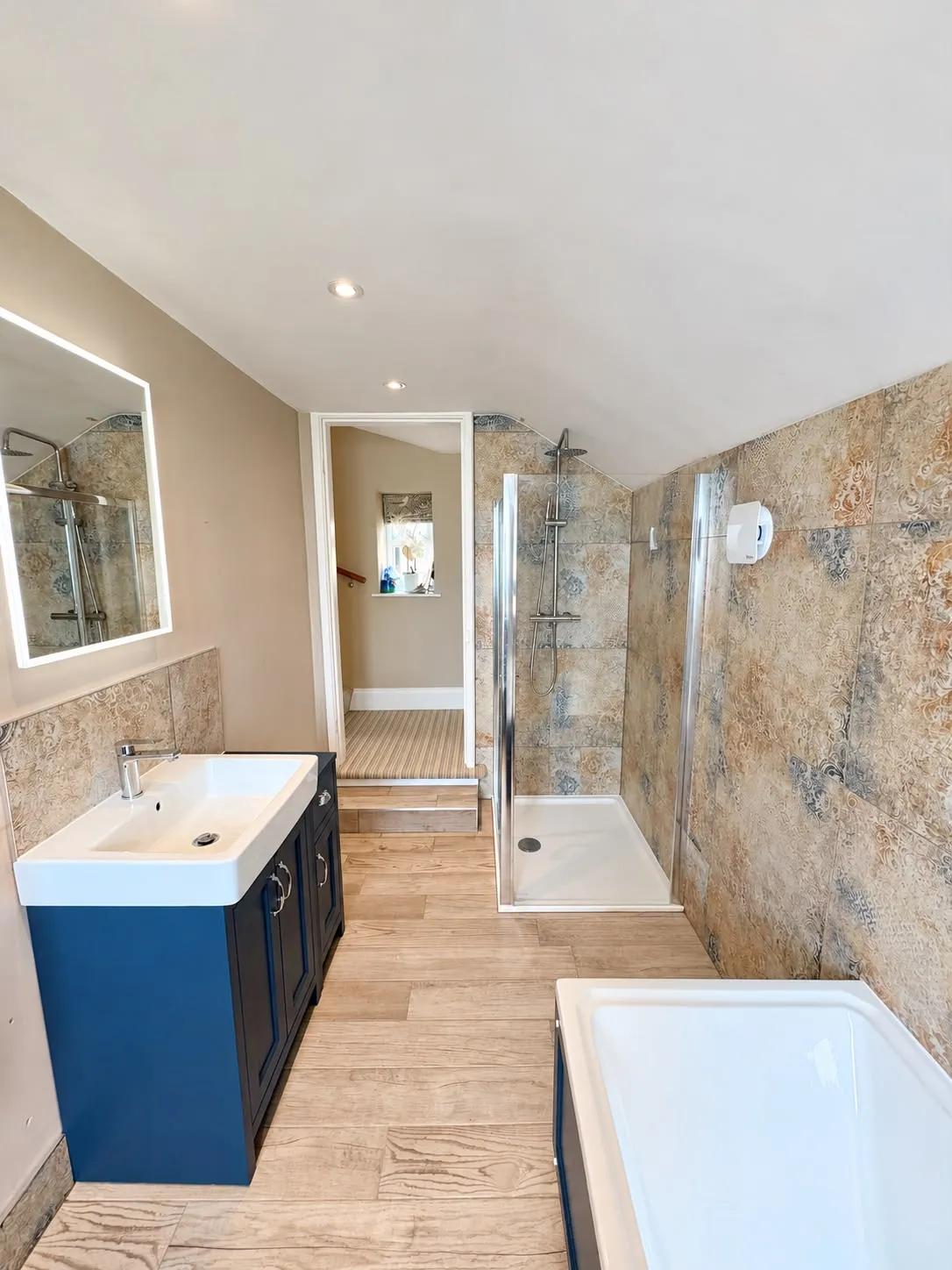 Same bathroom after: patterned wall tiles, new shower enclosure, blue vanity unit and wood-effect floor